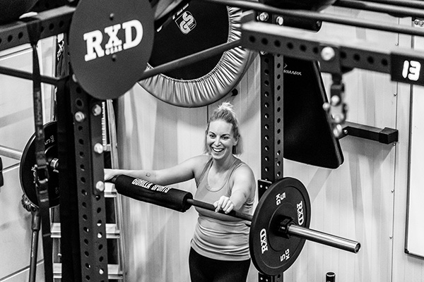 Zwart-wit foto van een lachende vrouw bij een halteroefening in een fitnessruimte